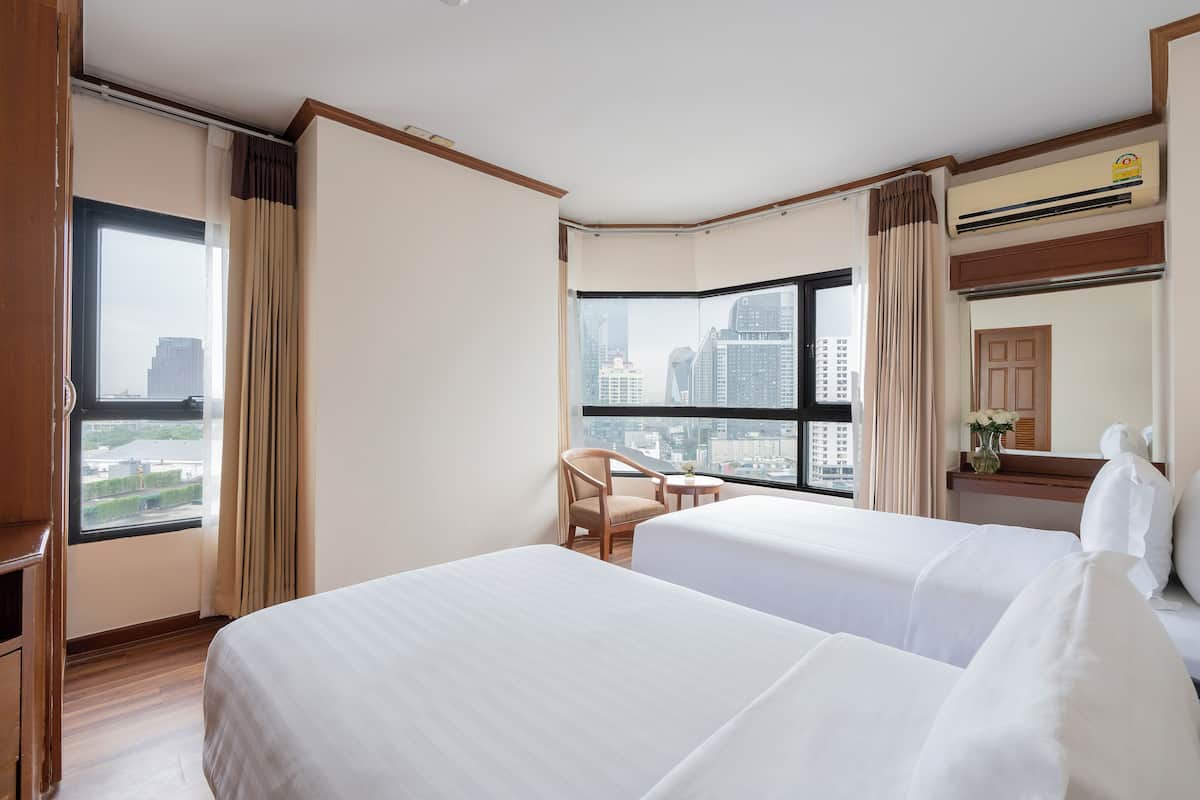 A hotel room with two beds, a chair, a small table, and a large window offering a city view.