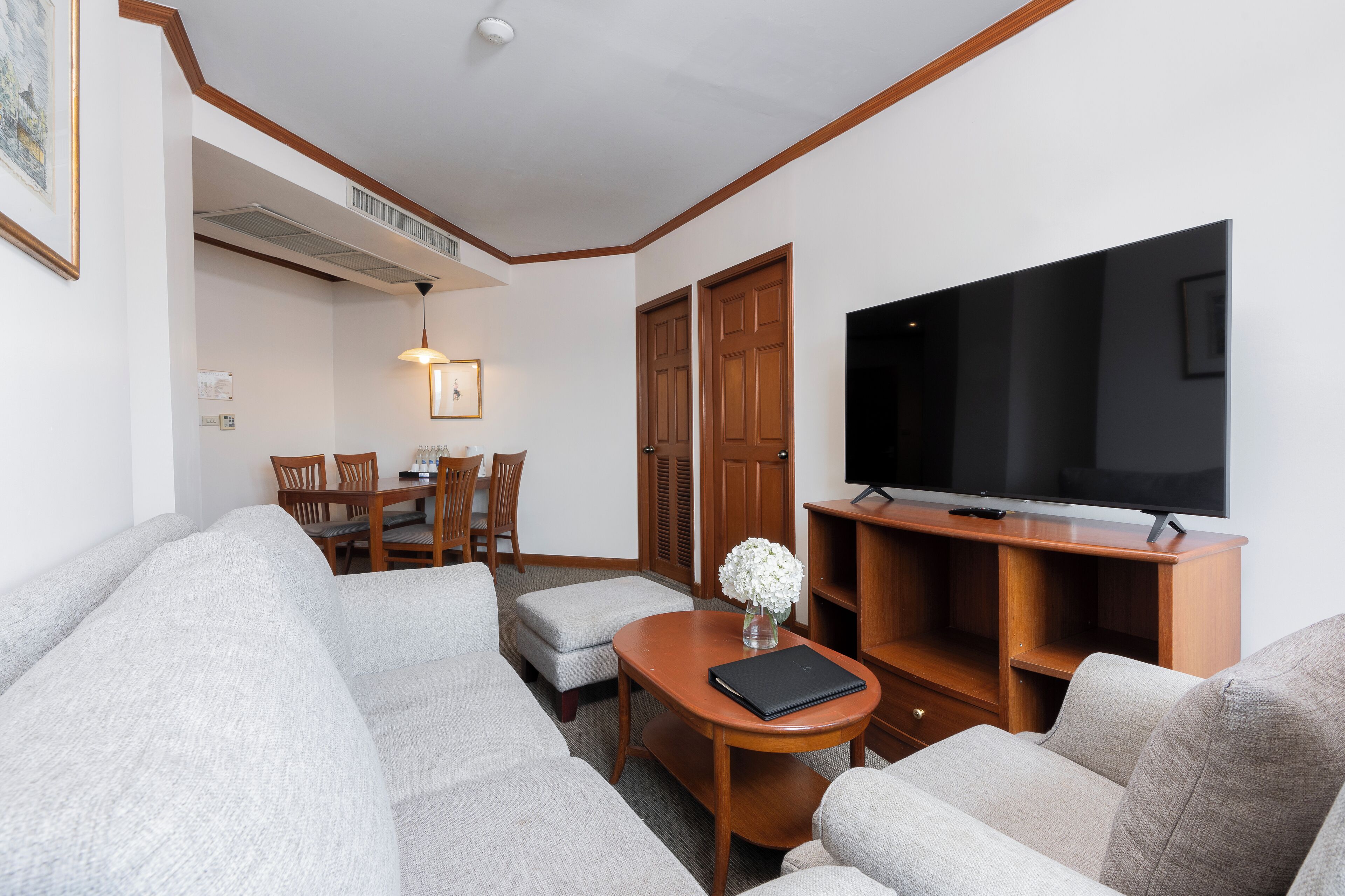 A living room with a sectional sofa, a coffee table, a TV on a wooden stand, a dining area with chairs and a table, and a hallway with a door.