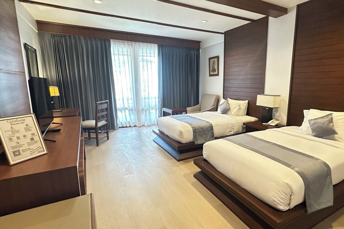Ein Hotelzimmer mit zwei Betten, einem Schreibtisch, einem Stuhl und einem großen Fenster mit Vorhängen.