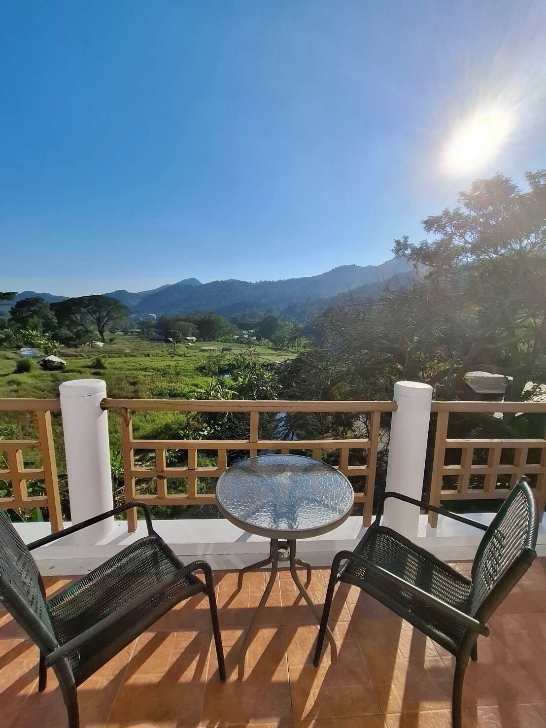 Un balcón con una mesa redonda y dos sillas, con vistas a un paisaje pintoresco con colinas y árboles.