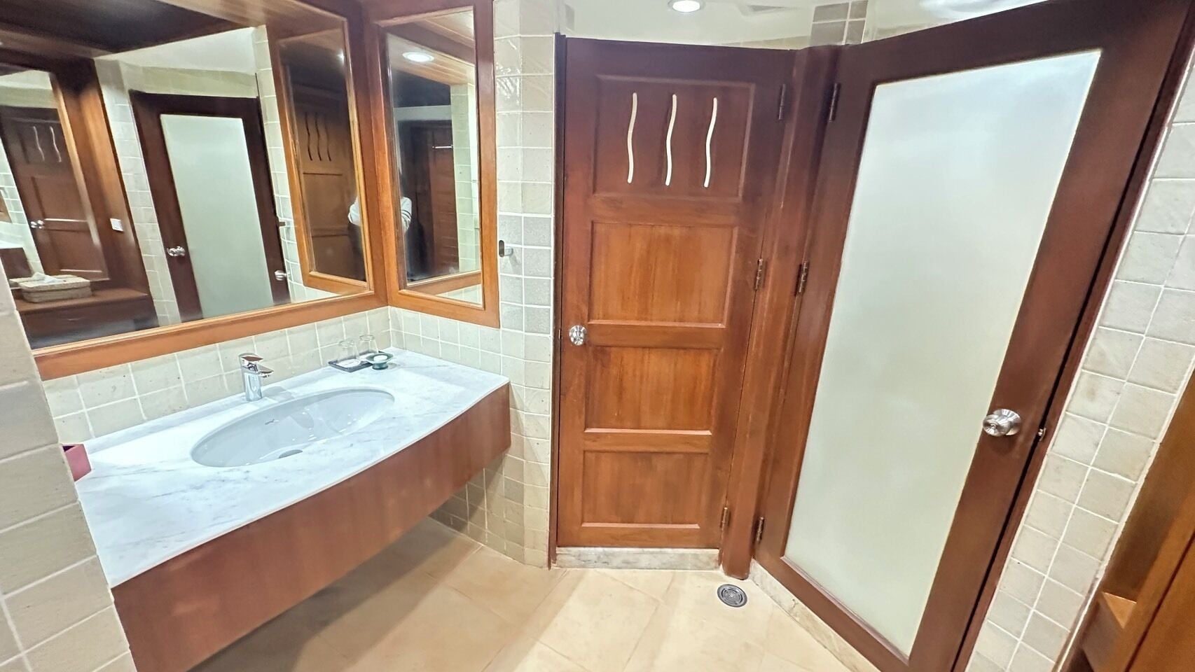 A bathroom with a marble sink, wooden vanity, and a frosted glass door.