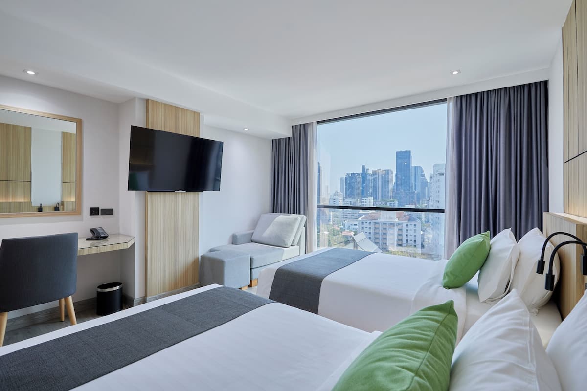 Une chambre d’hôtel avec deux lits, un bureau, une chaise, une télévision et une vue sur les toits de la ville.