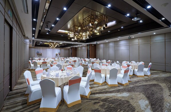 Une salle de banquet dotée de tables rondes et de chaises blanches, agrémentées de rubans dorés, dans un décor moderne avec un lustre et un éclairage encastré.