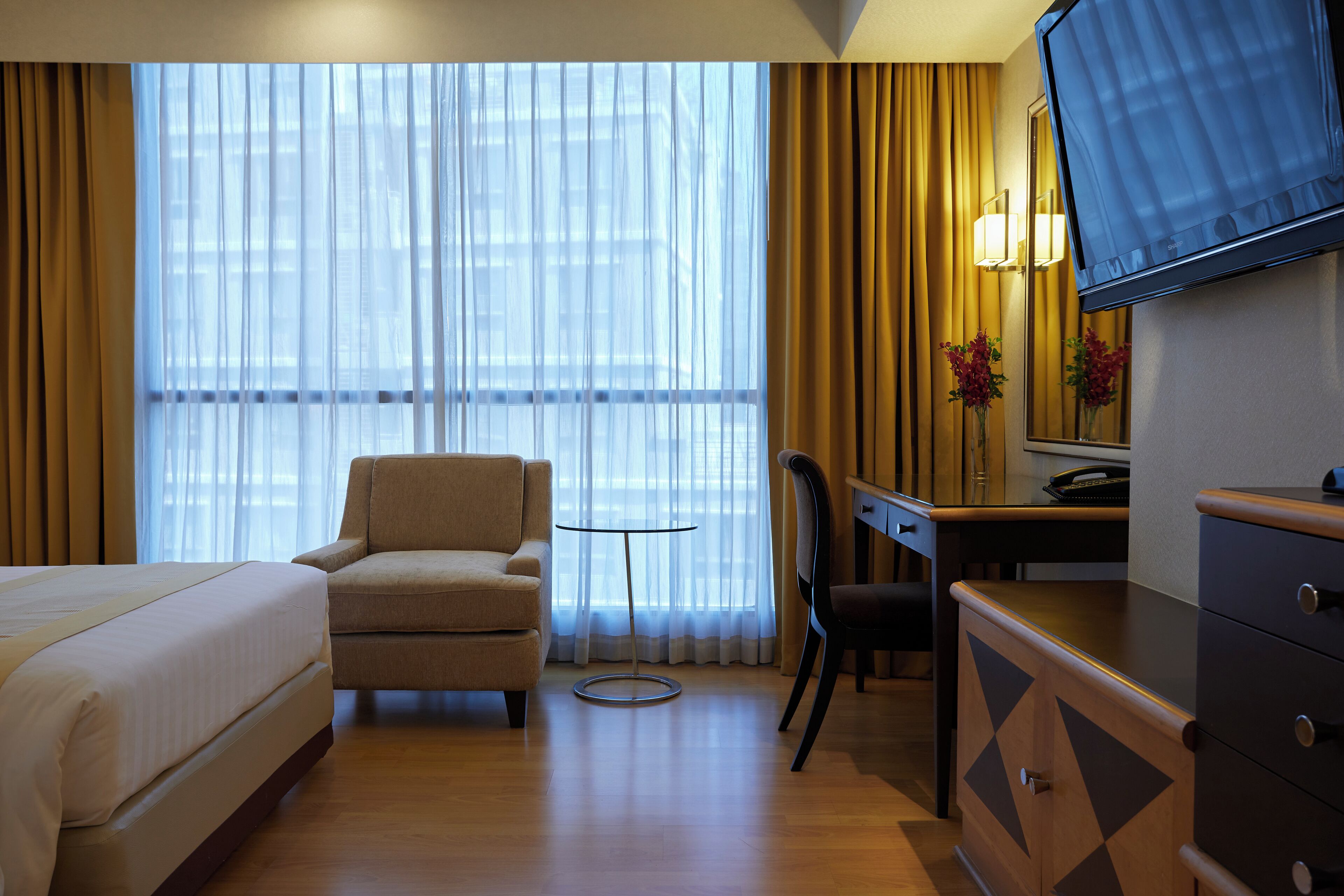 Een hotelkamer met een bed, een stoel, een bureau, een televisie en een raam met gordijnen.