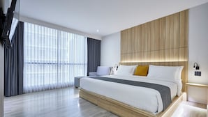 Quarto de hotel moderno com uma cama grande, cabeceira de madeira e uma janela ampla com cortinas.
