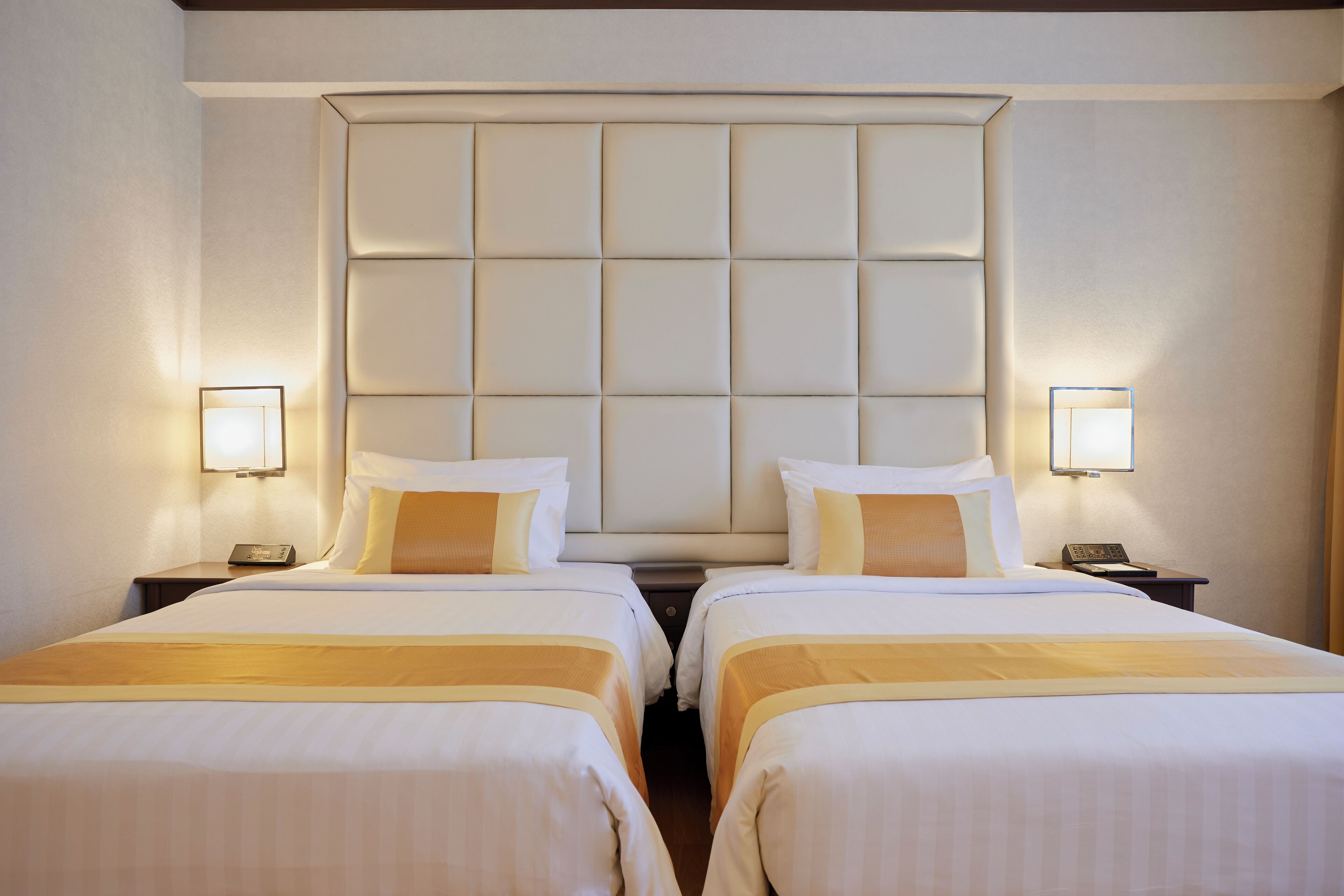 Habitación de hotel con dos camas, cabecero acolchado, lámparas de noche y teléfono en cada mesita.