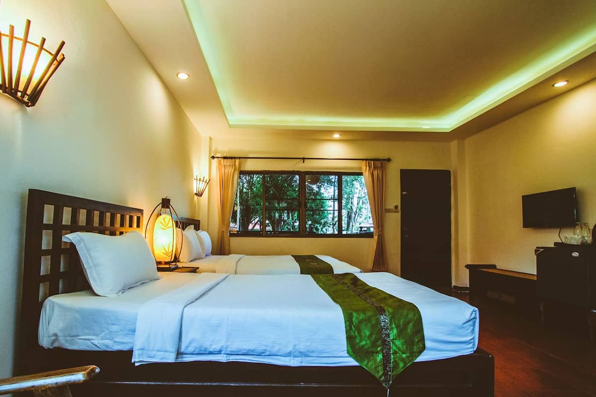 A hotel room with two beds, a TV, a desk, and a window with curtains.
