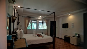A four-poster bed with a wooden frame, a flat-screen TV mounted on the wall, and a small table with a chair. - Baan Thai Resort (Chiang Mai)