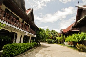 A traditional wooden building with a balcony, surrounded by lush greenery and a clear sky.
