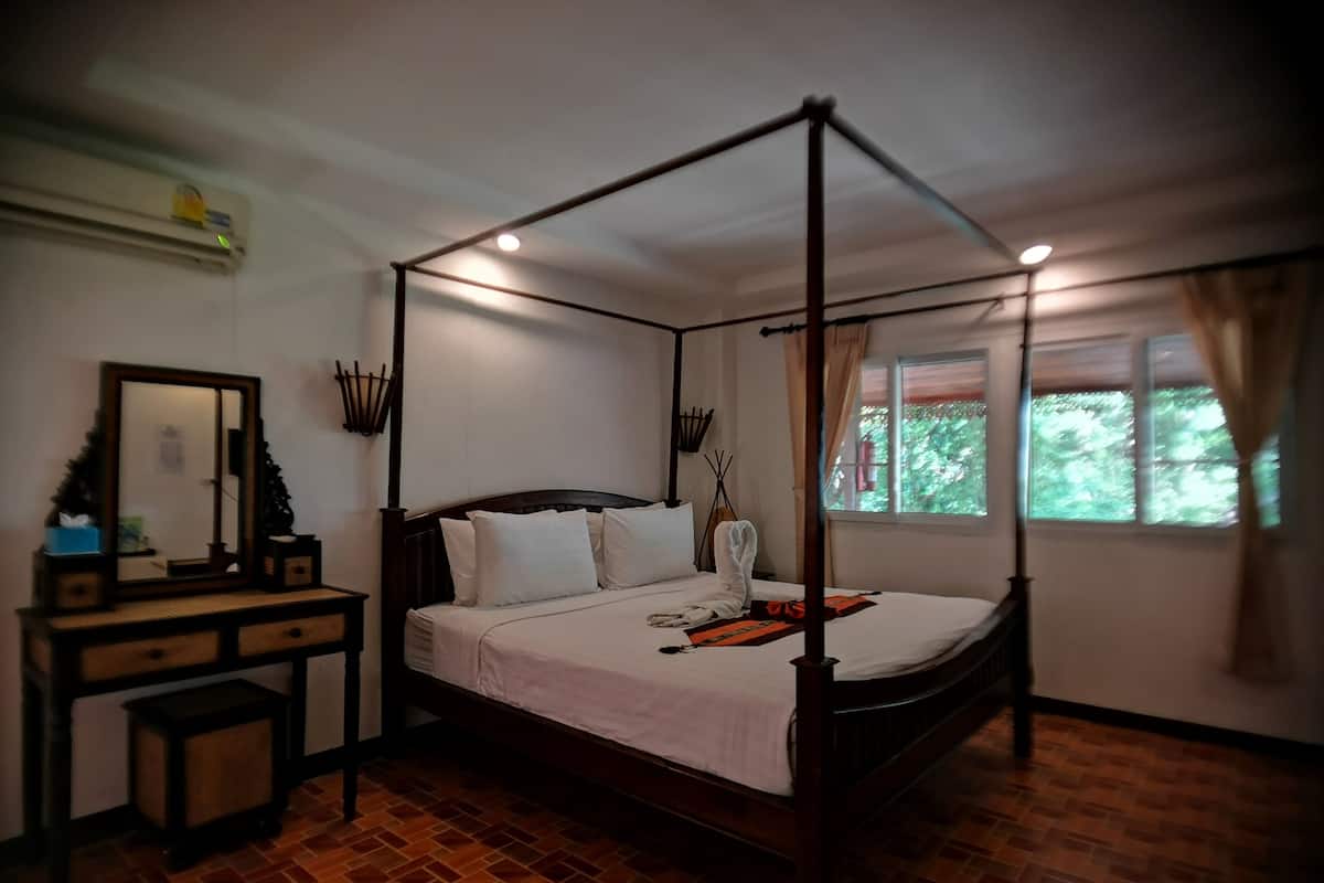 A four-poster bed with white bedding, a wooden nightstand, a mirror, and a window with curtains.