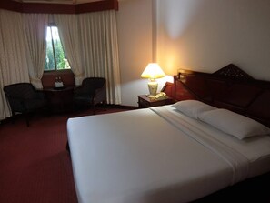 A hotel room with a large bed, a desk with a chair, a lamp, and a window with curtains. - Inn Come Hotel Chiangrai (Chiang Rai)
