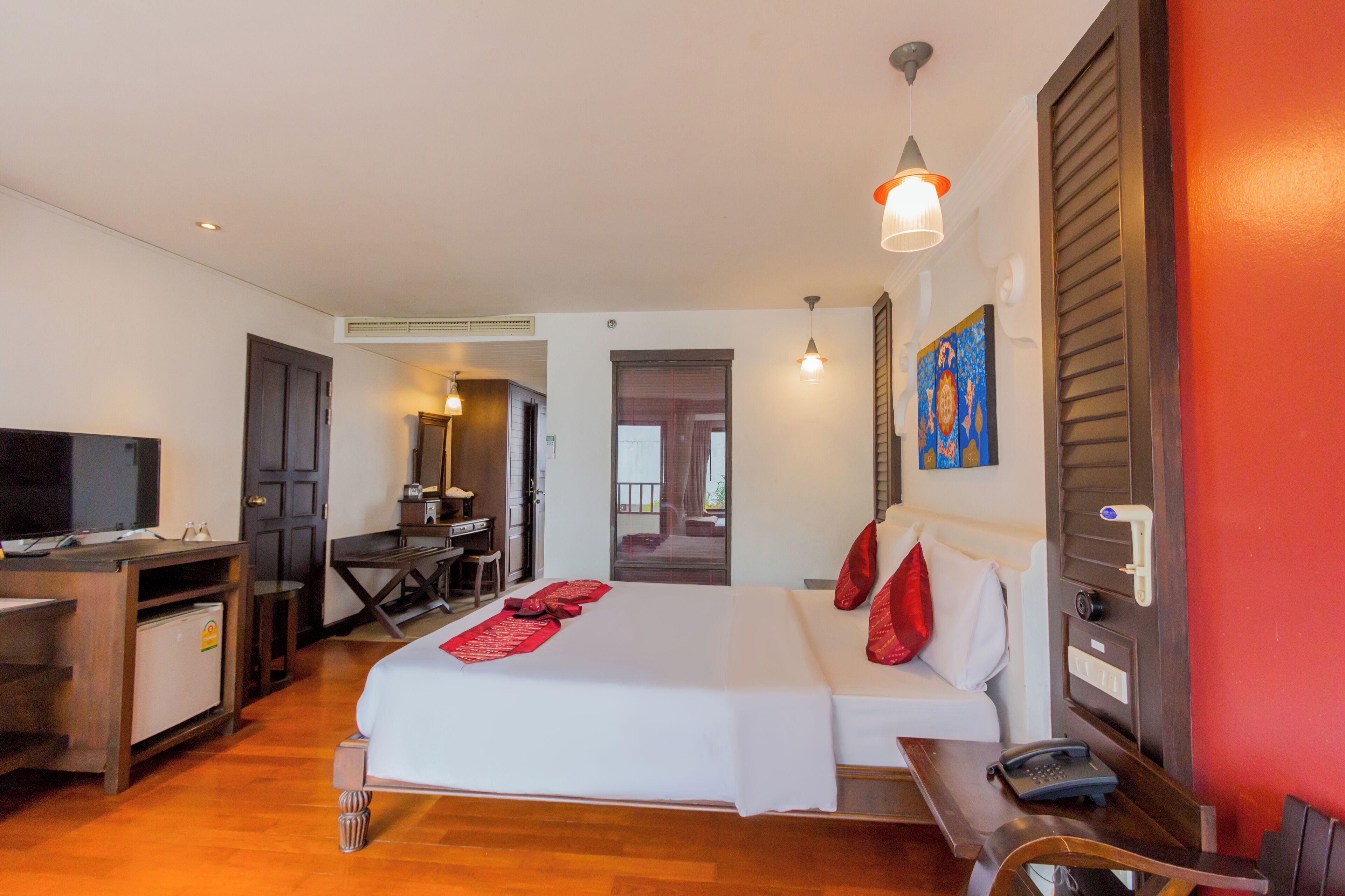 A hotel room with a bed, a desk, a television, and a door leading to a balcony.
