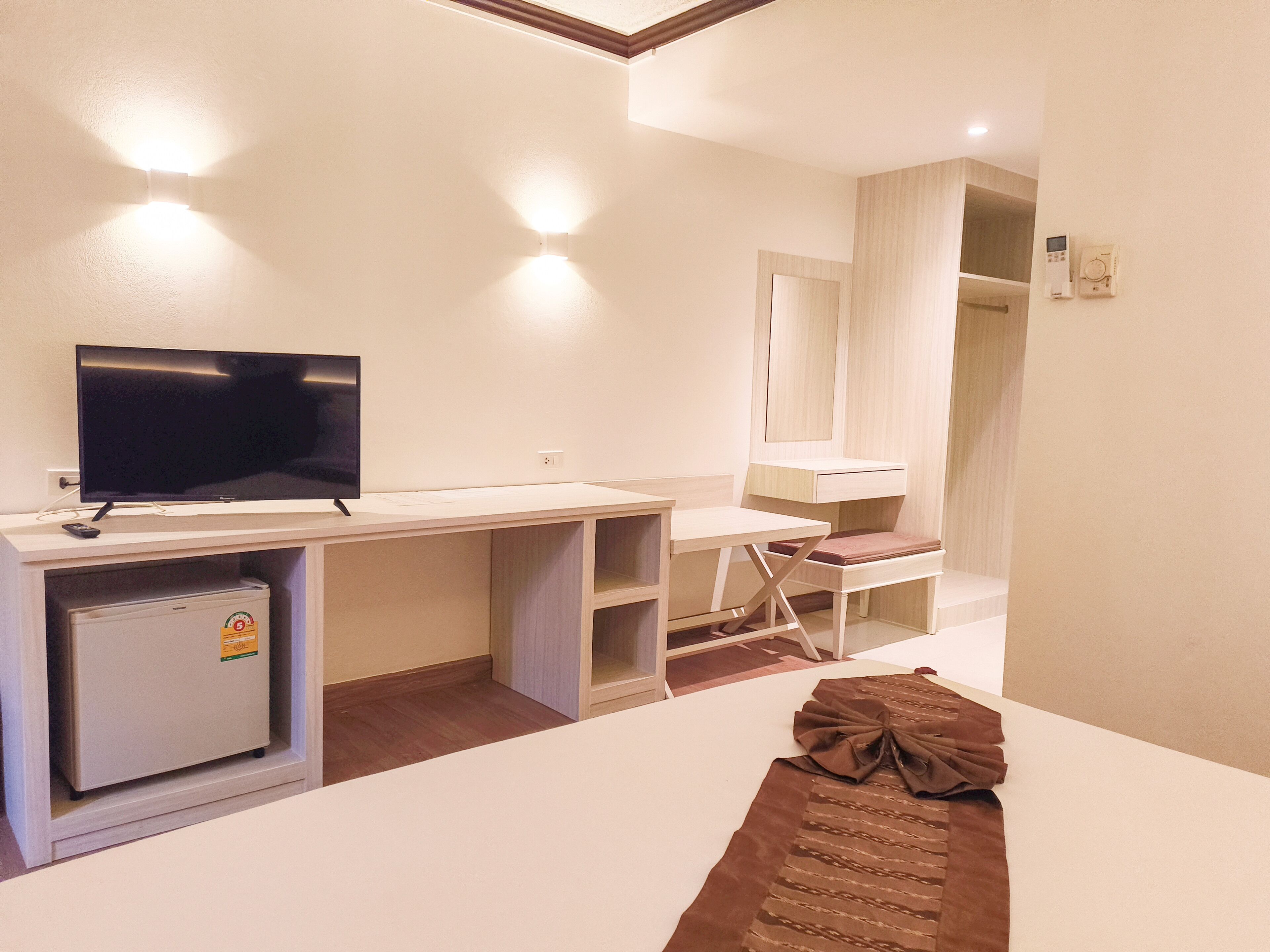 A hotel room with a flat-screen TV, a small refrigerator, a desk, and a mirror.