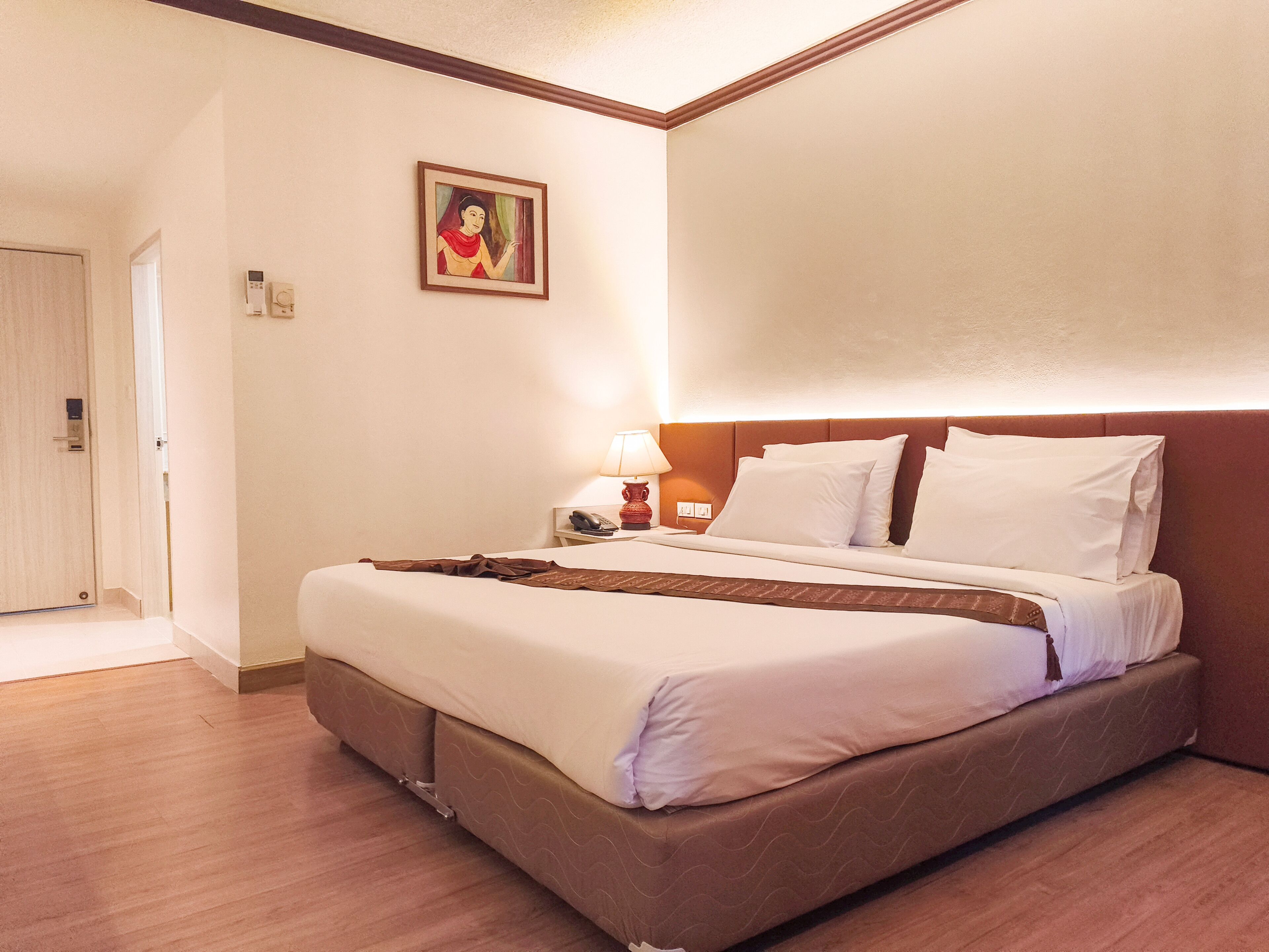 A hotel room with a bed, bedside table, lamp, and a painting on the wall.