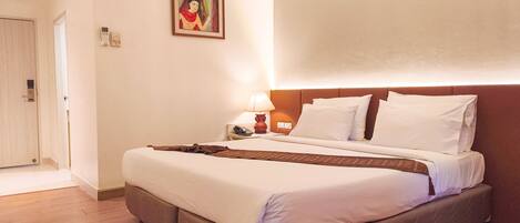 A hotel room with a bed, bedside table, lamp, and a painting on the wall.