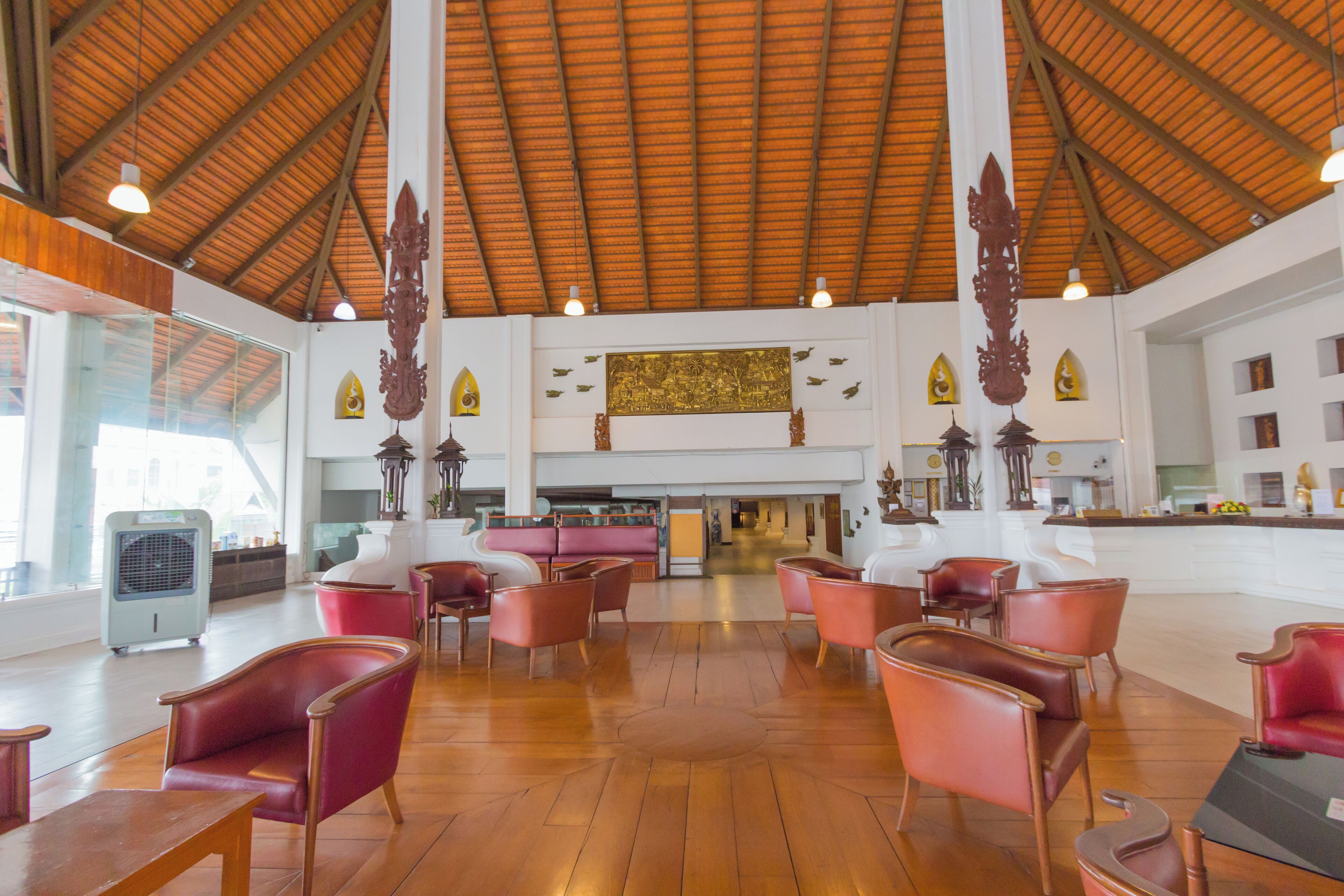 A spacious lobby with high ceilings, wooden flooring, and red leather chairs.