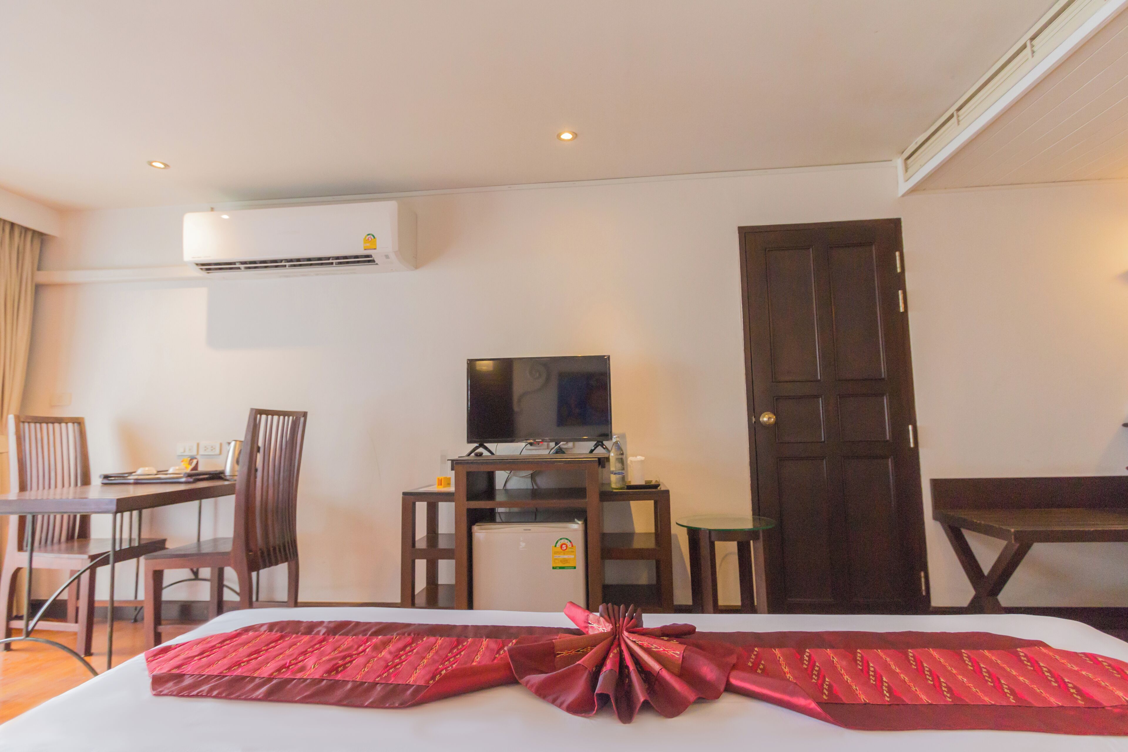 A hotel room with a bed, a desk with a television, a refrigerator, and a dining area with chairs.