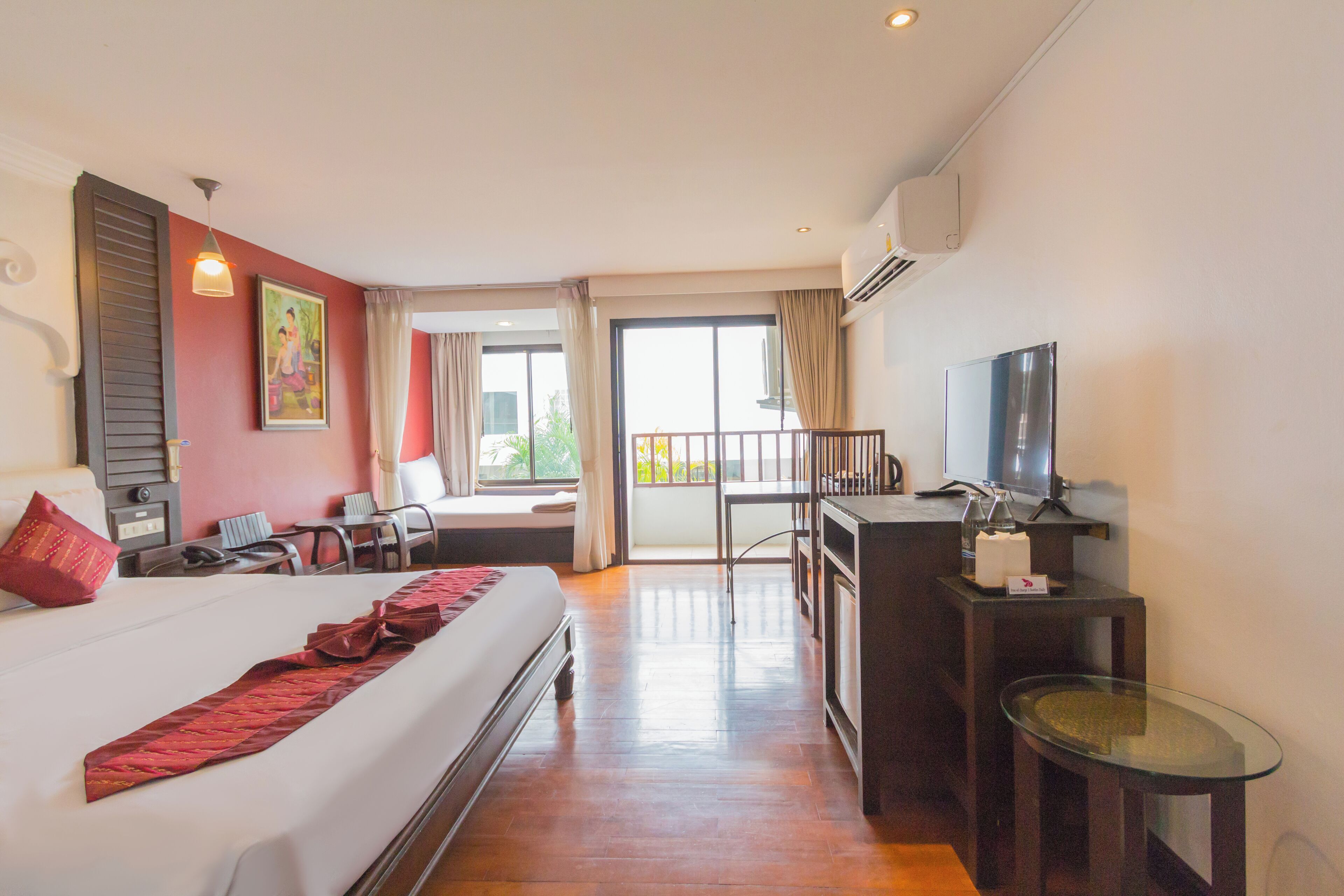 Habitación de hotel con una cama grande, un escritorio con silla, televisor y balcón con barandilla.