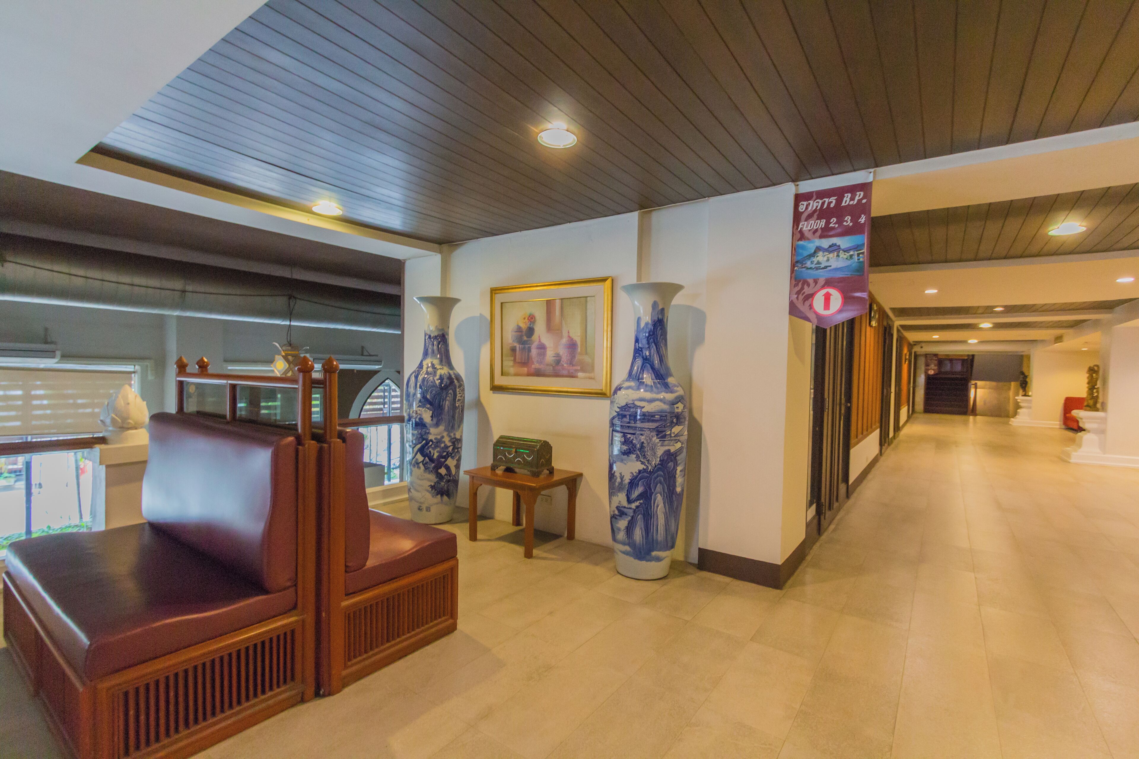 Um hall com área de estar, vasos grandes, um quadro emoldurado e uma placa com texto.