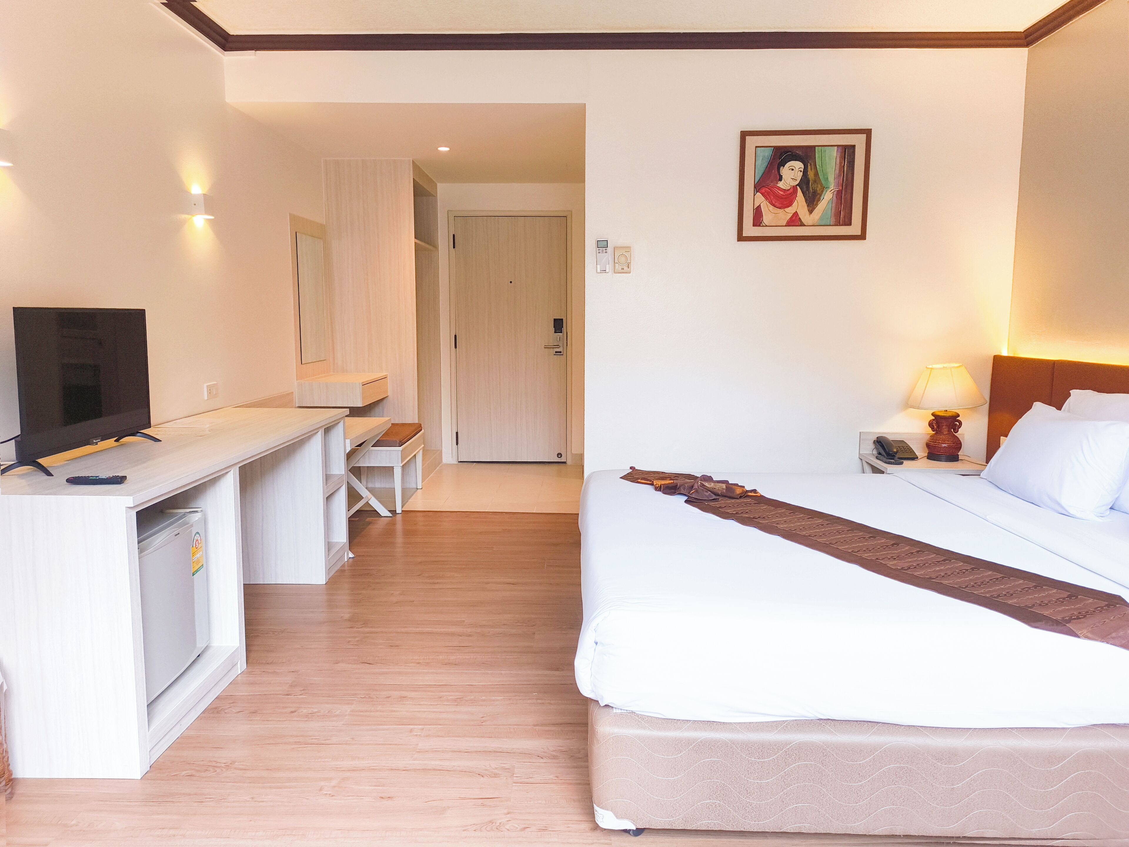 A hotel room with a bed, a desk, a television, a lamp, and a painting on the wall.