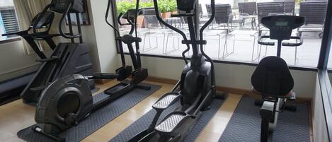 Un gimnasio con diferentes máquinas de cardio, colchonetas y vistas a una zona de estar exterior.