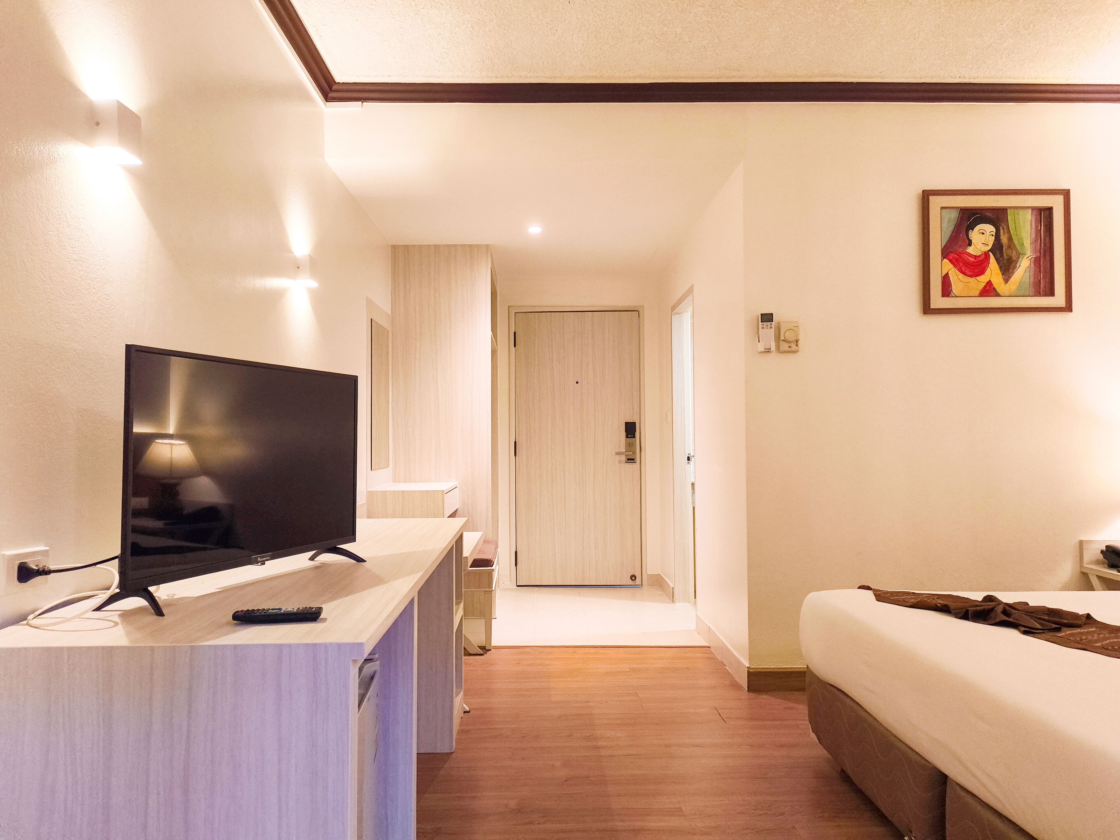 A hotel room with a TV, bedside table, bed, and a painting on the wall.