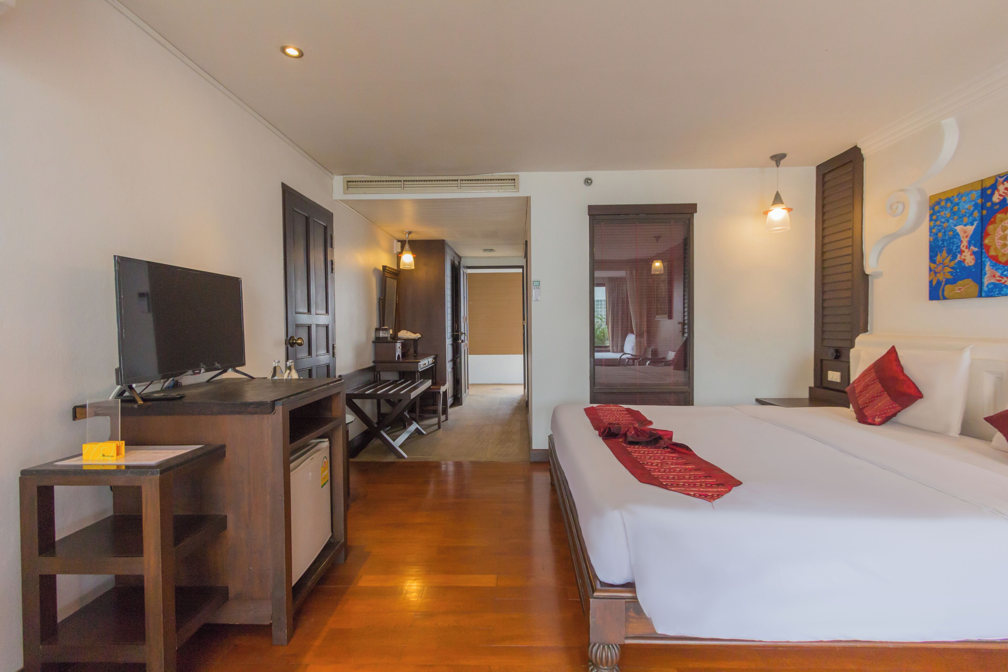 Habitación de hotel con cama, escritorio, televisor y baño visible a través de una puerta abierta.