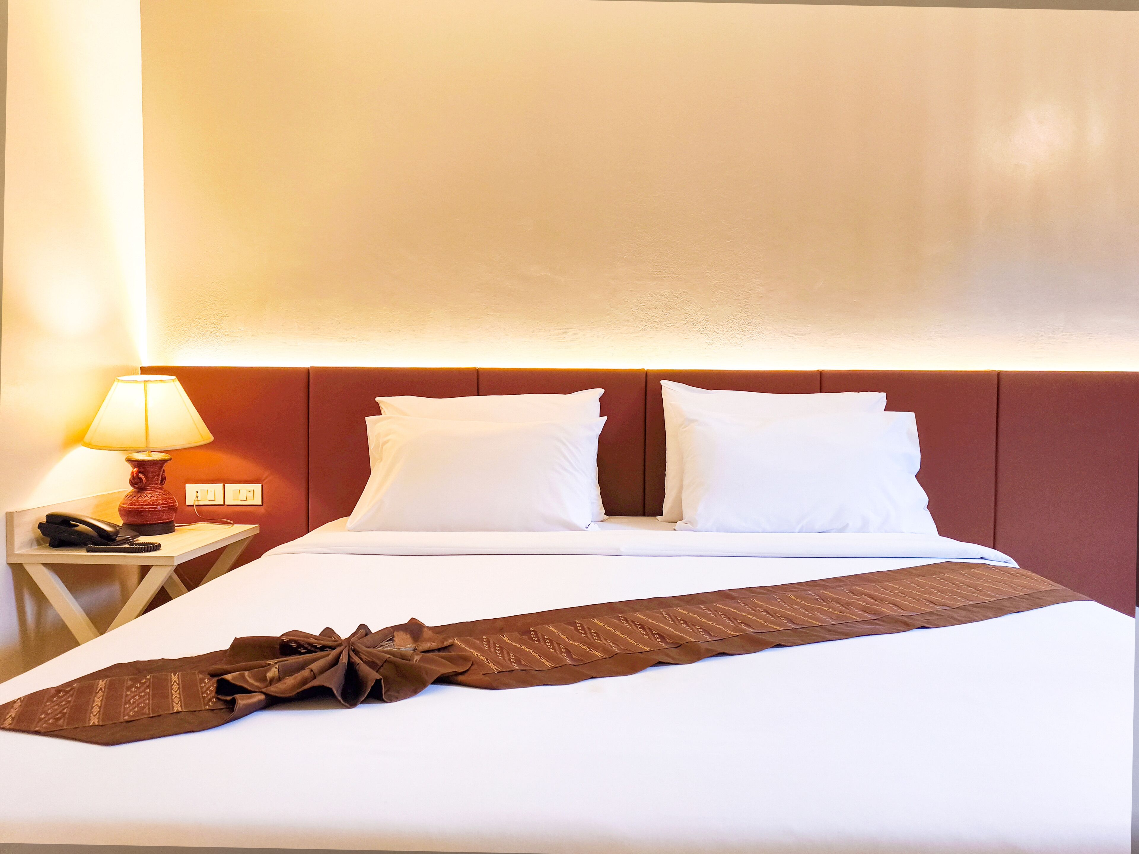 A hotel room with a bed, pillows, a bedside lamp, a telephone, and a tie on the bed.