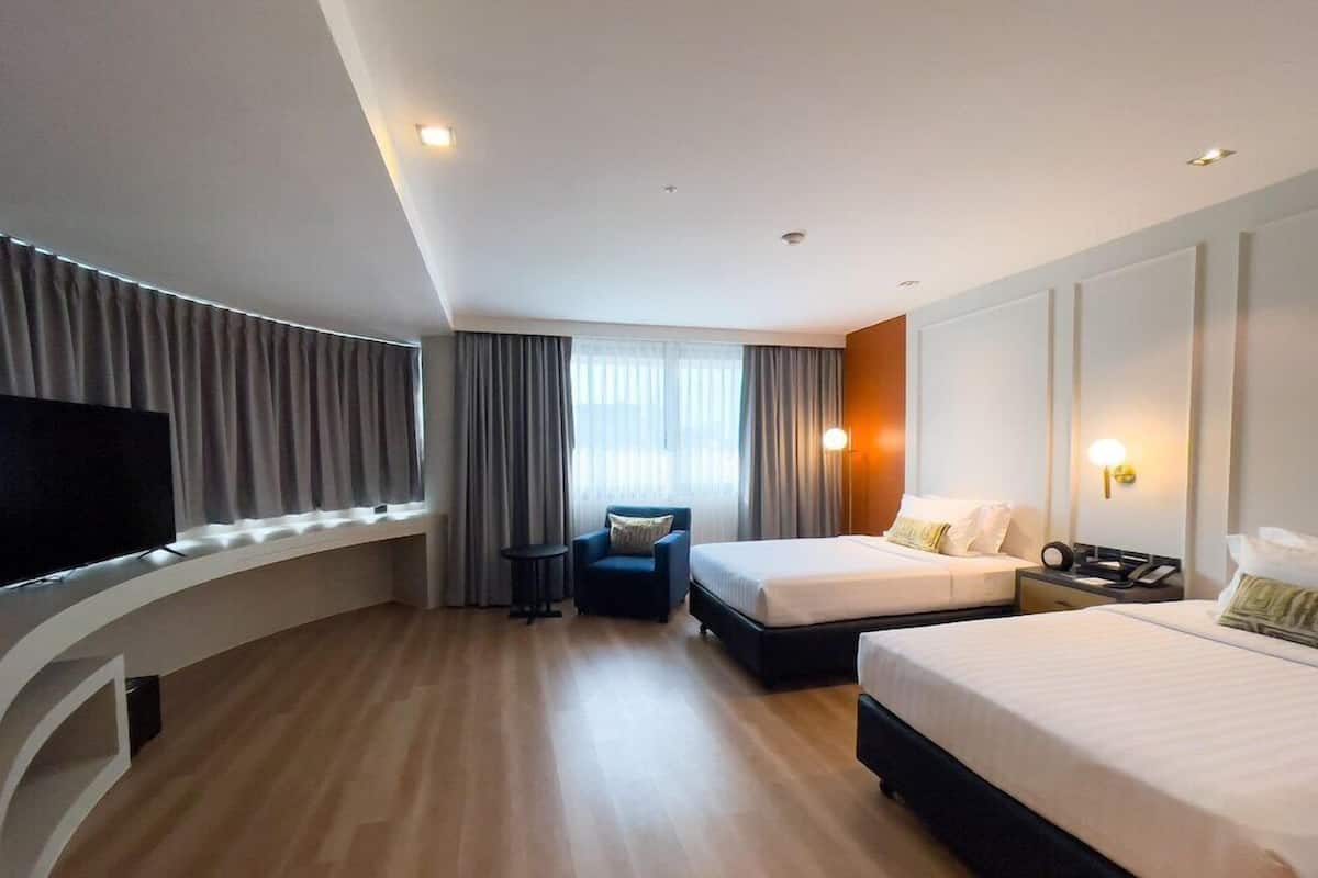 A modern hotel room with two beds, a TV, a desk, and a sofa.
