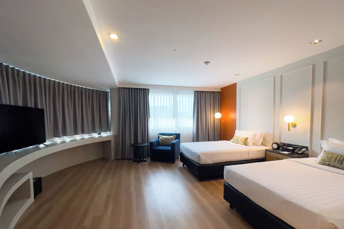 A modern hotel room with a large bed, a smaller bed, a desk, a chair, and a TV.