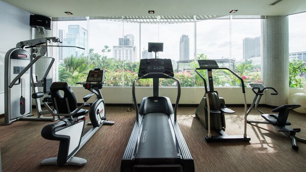 Uma academia com máquinas de cardio, aparelhos de musculação e uma grande janela com vista para a cidade.