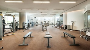 Uma academia ampla com diversos equipamentos de exercício, bancos e espelhos.
