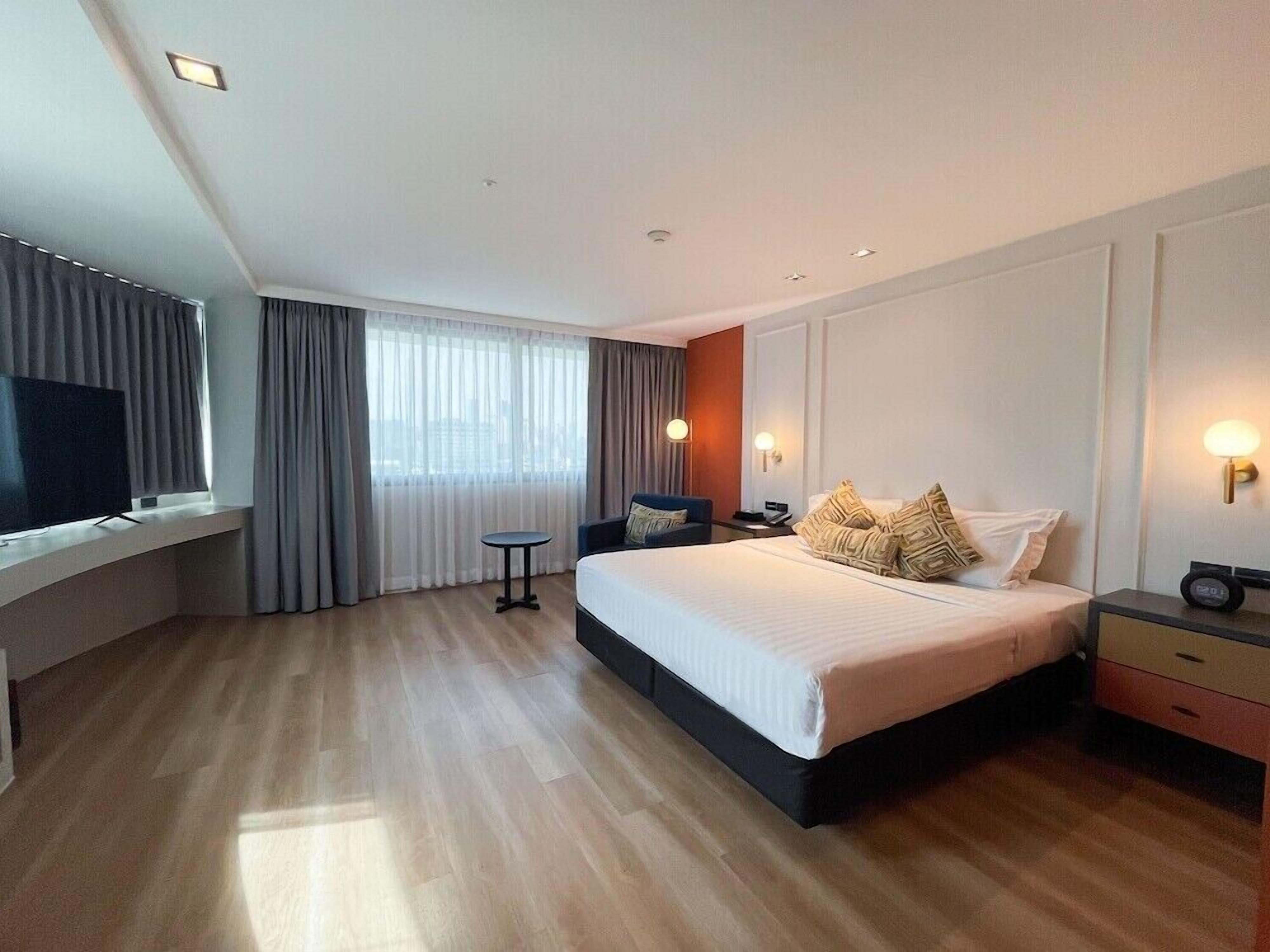 Een moderne hotelkamer met een groot bed, een televisie op een inbouwplank, een klein tafeltje en een raam met gordijnen.