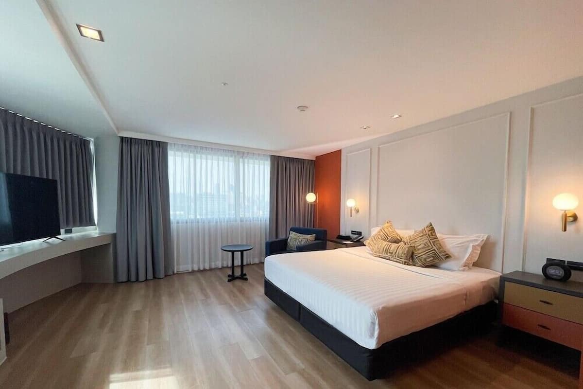 A modern hotel room with a large bed, a TV on a built-in shelf, a small table, and a window with curtains.