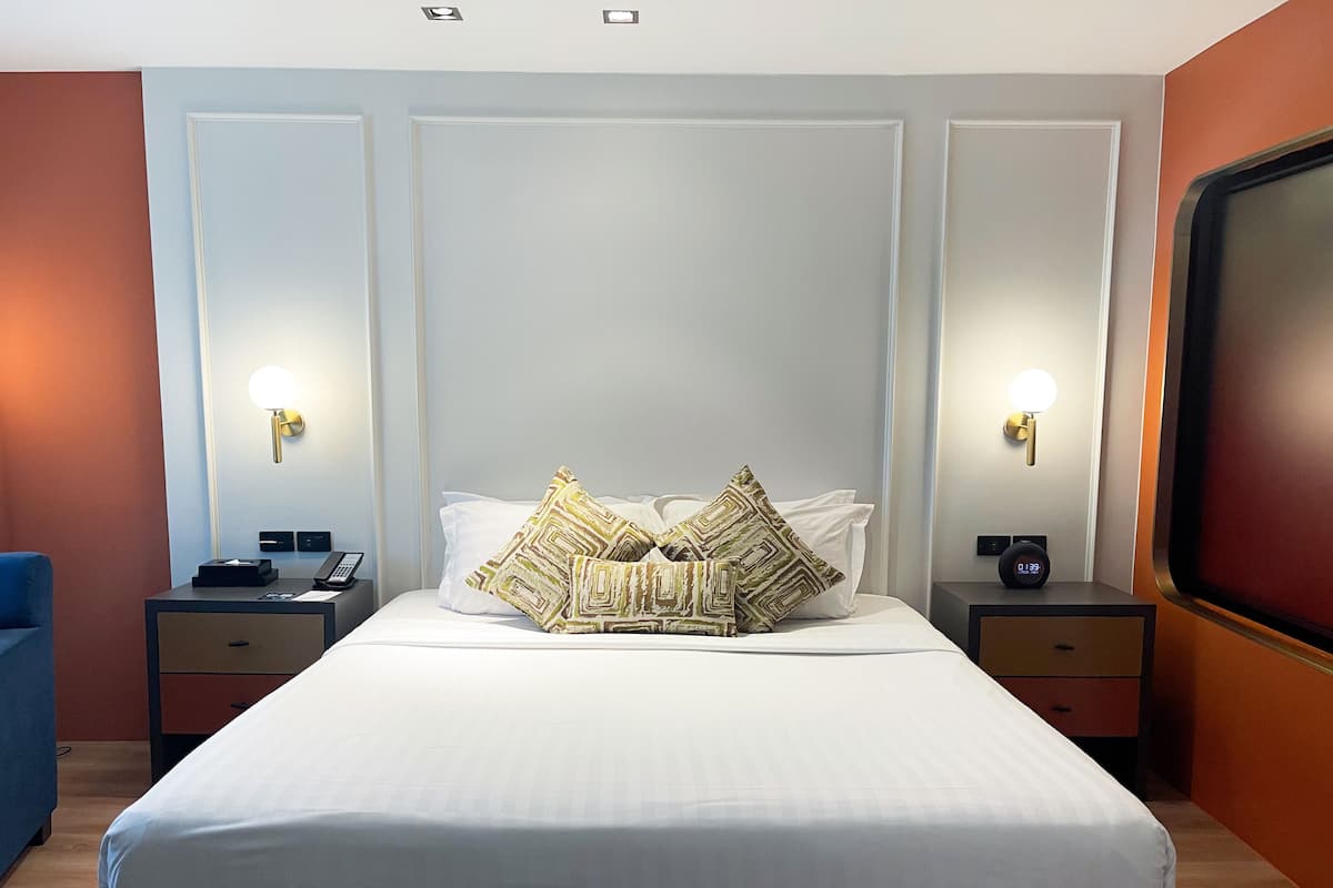 A hotel room with a large bed, two bedside tables with lamps, a blue chair, and a large TV on the wall.