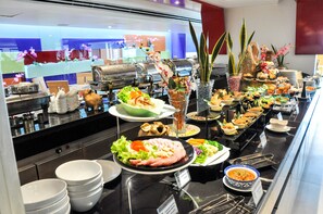 A buffet with various dishes, including salads, meats, and desserts, arranged on a counter with a kitchen in the background. - Gold Orchid Bangkok (Bangkok)