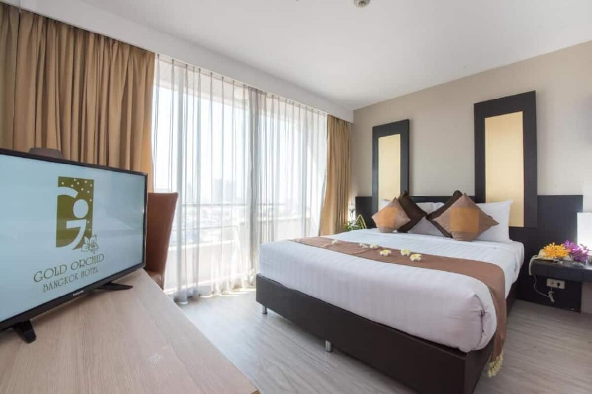 A hotel room with a bed, a TV, a desk, and a window with curtains.