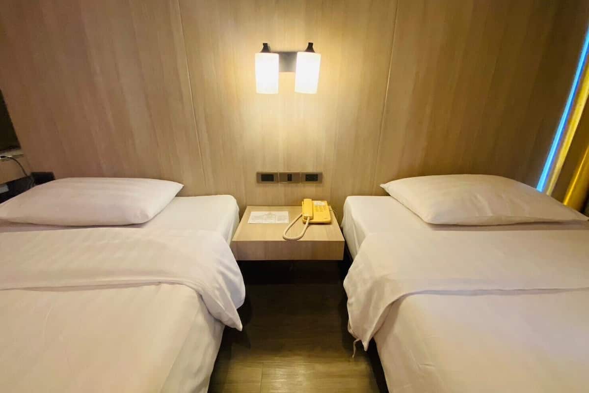A hotel room with two single beds, a bedside telephone, and a wall-mounted light fixture.