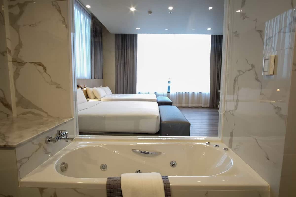 A modern hotel room with a large bathtub, a bed with two pillows, and a view of the city.
