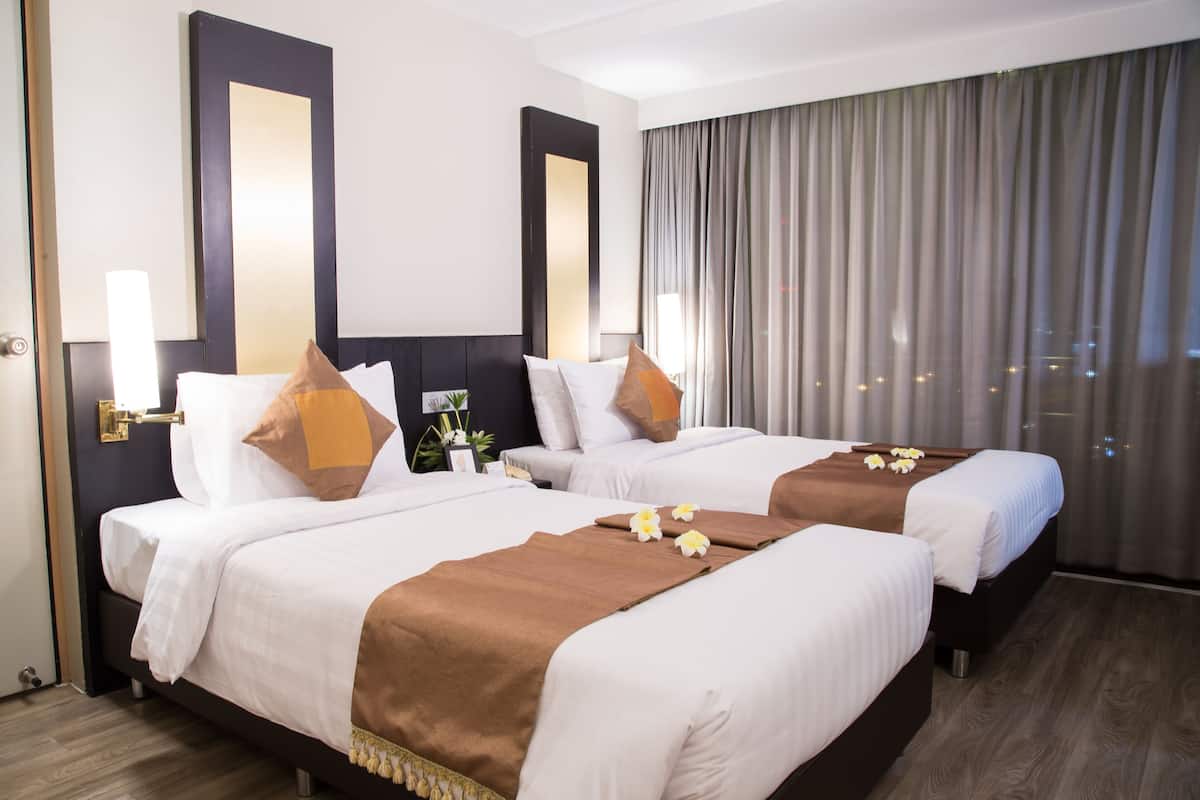 A hotel room with two beds, a large window with curtains, and a view of the city.