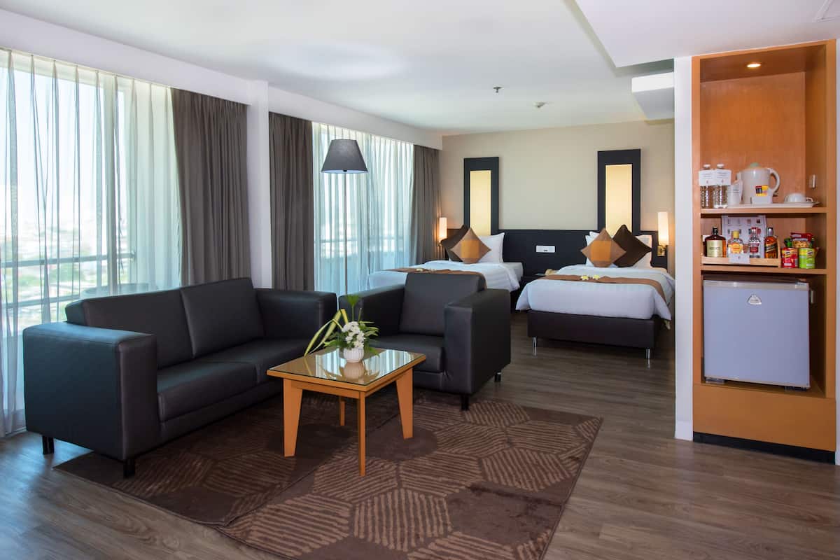 A hotel room with a sofa, a bed, a small table with a vase, and a mini-fridge.