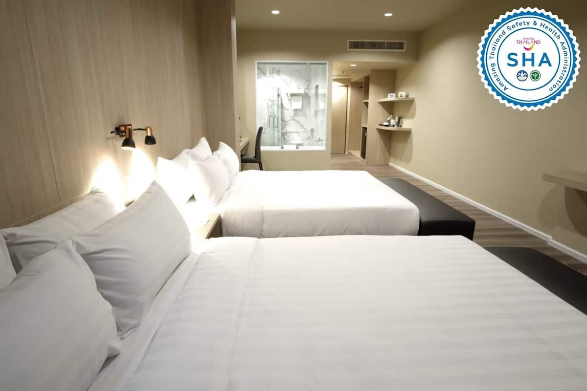 A hotel room with two beds, a desk, a chair, and a window.