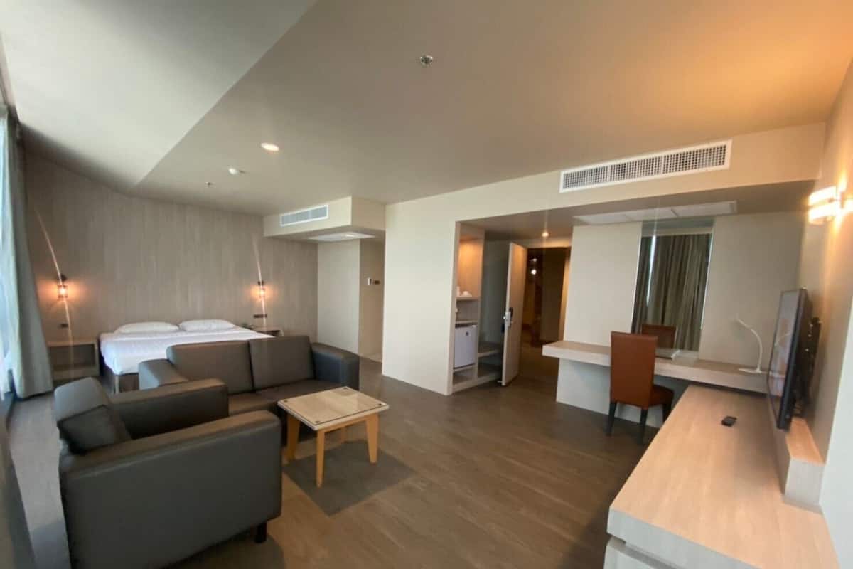 A modern hotel room with a bed, sofa, coffee table, and a kitchenette area.