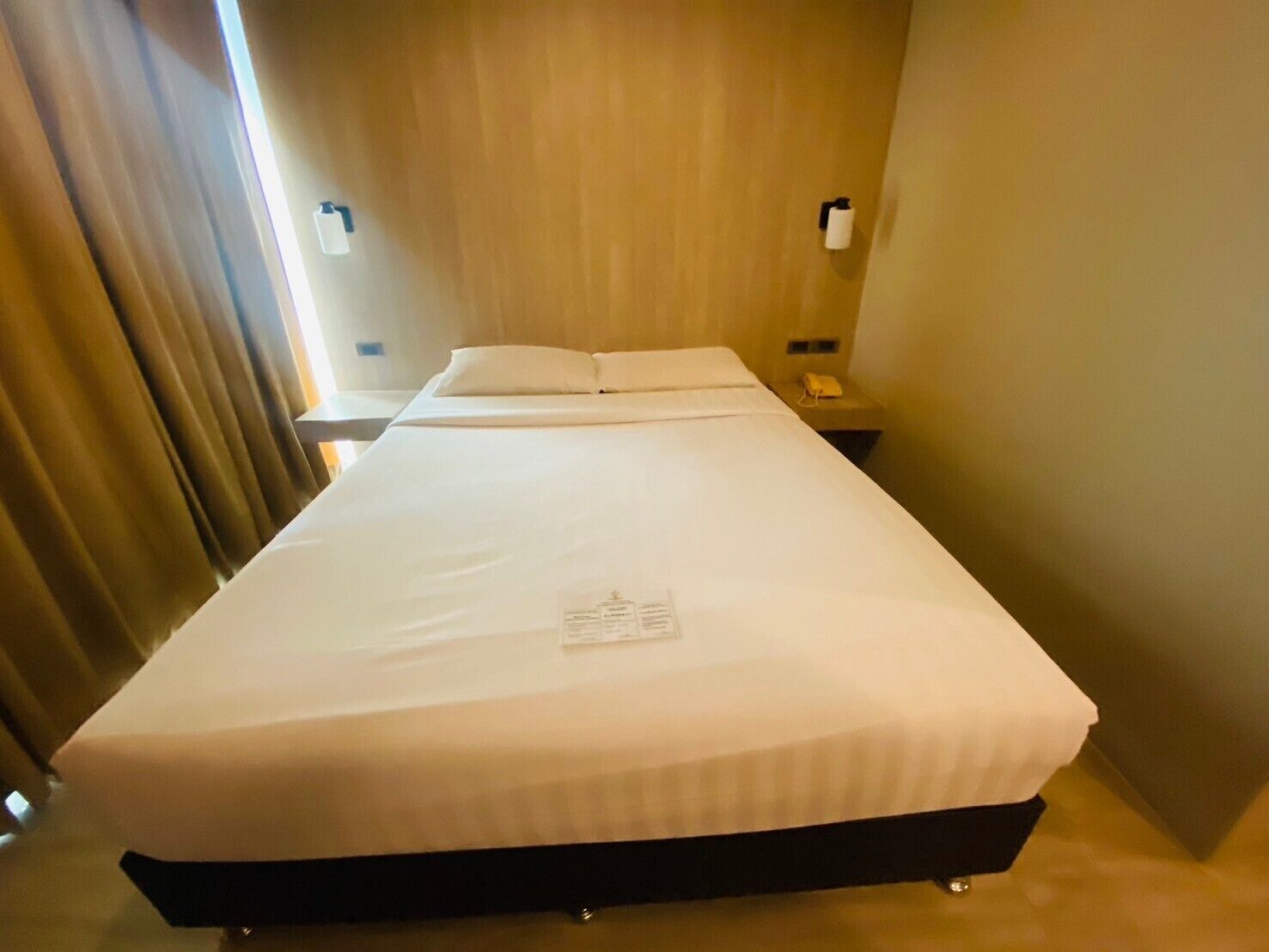 Une chambre d’hôtel avec un grand lit, une table de chevet, une lampe et un rideau.