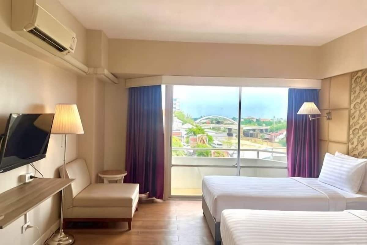A hotel room with a bed, a TV, a desk, a chair, and a view of the city.
