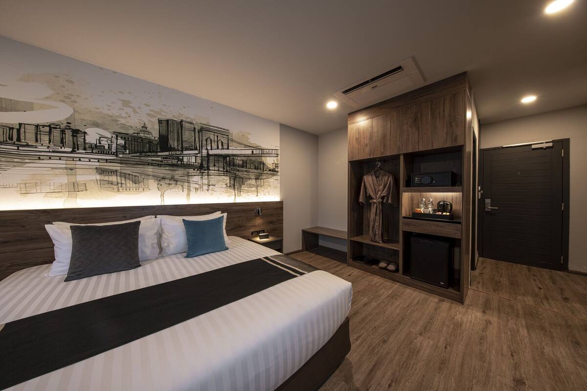 Habitación de hotel moderna con una cama grande, un mural de la ciudad, un vestidor y una puerta de madera oscura.