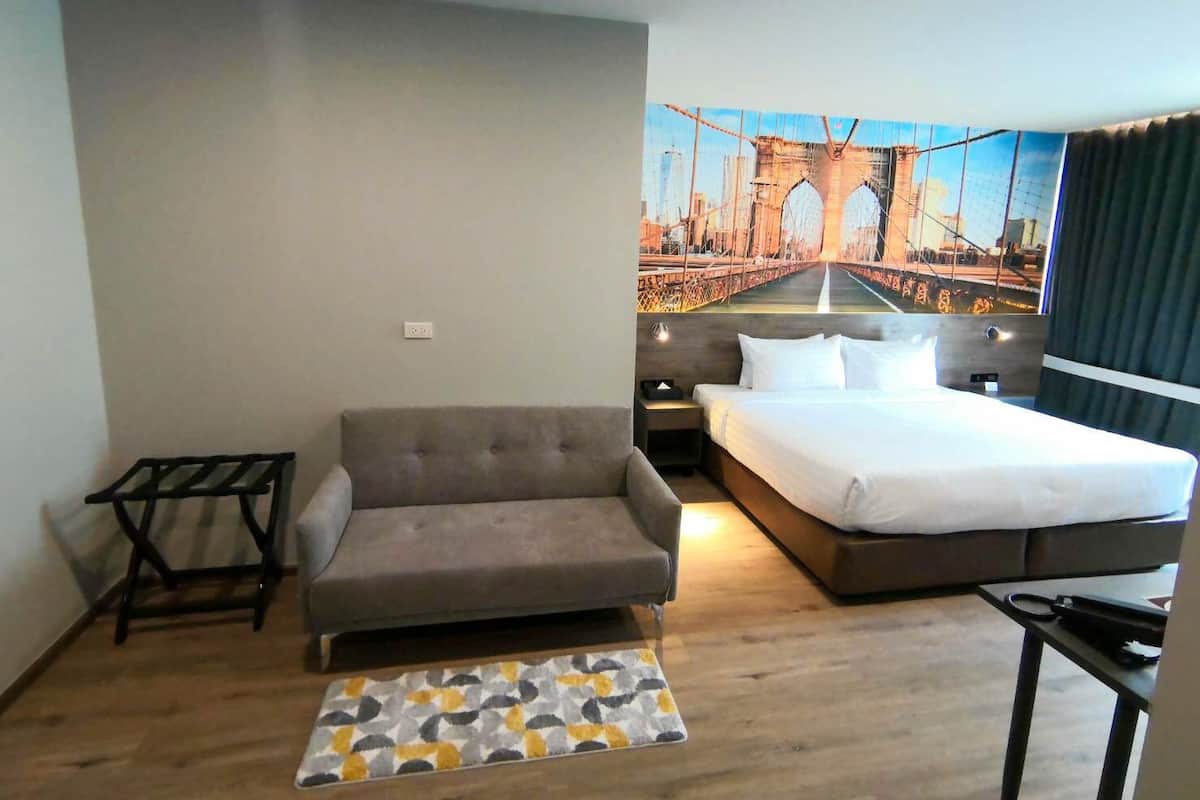 Una habitación de hotel con un sofá, una cama, una mesita y una alfombra.