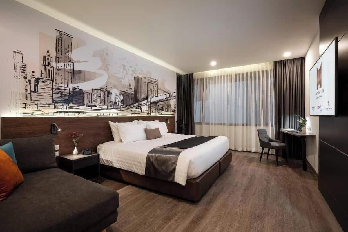 Habitación de hotel con cama, sofá, escritorio y un gran mural de paisaje urbano en la pared.