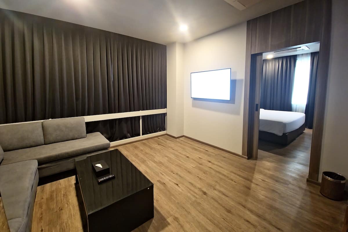 Una habitación de hotel moderna con sofá gris, una mesita de centro negra, un televisor de pantalla plana en la pared y piso de madera.