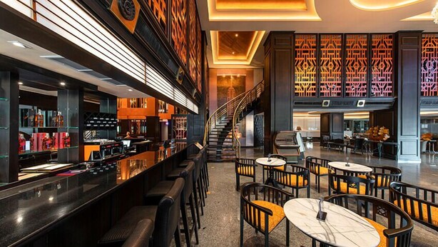 A modern bar area with a long counter, multiple seating options, and a staircase leading to an upper level. - Manhattan Bangkok (Bangkok)